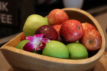Apples in a wooden bowl with orchid flower in the background