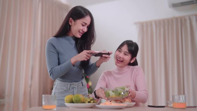 Asian female friends capture memories by taking photos together using smartphones at the dining table in the festive atmosphere of Christmas at her home