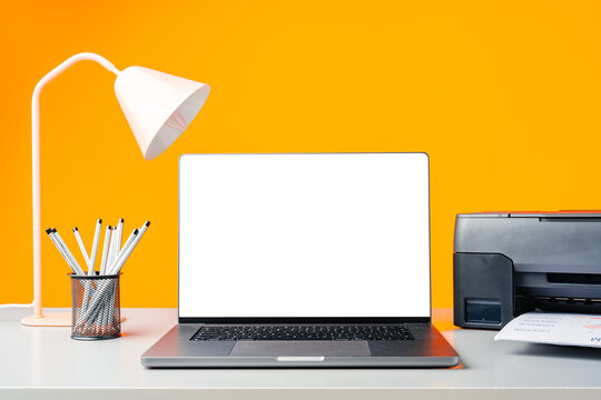 Laser printer and laptop on desk against yellow background
