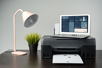 Modern printer with paper and laptop on table in office