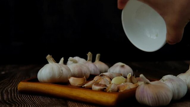 A man's hand pours garlic cloves onto a wooden plate.