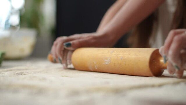 Close-up of the hands of a mother and daughter using a rolling pin to roll out dough on the table. Home cooking as a way to prepare something healthy and tasty