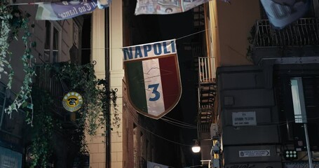 Napoli football crest displayed in city alley, night scene. Italy