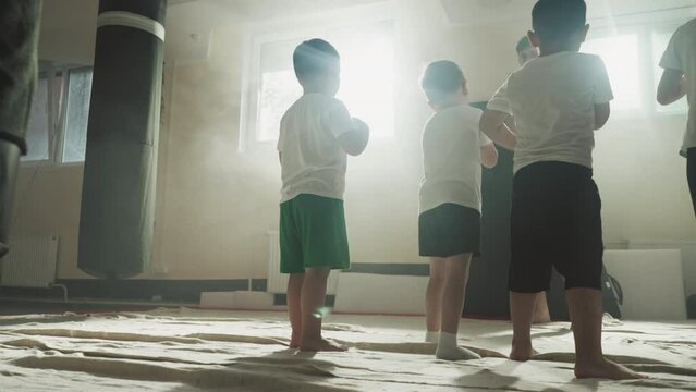Children do hits with instructor at boxing school. Little fighters exercise strong punches with professional trainer in gym slow motion. Self-defence lesson
