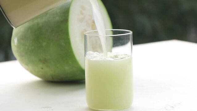 A glass of Ash gourd or wax gourd Juice in focus with Raw ash gourd in background.