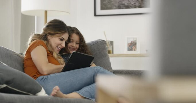 Mother, child and tablet on couch, app and streaming series or cartoon movie. Mom, daughter and digital technology on sofa, social media and funny joke or online humor, conversation and chat or game