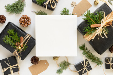 Paper card between Christmas decorations, gift boxes and green fir branches, mockup
