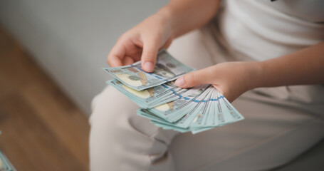 Portrait close up of young asian woman counts cash dollar bills while sitting in living room at...