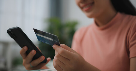 Portrait close up of Young asian woman sitting on sofa in living room, makes online banking payments through the internet from bank card on smartphone ,Shopping online with credit card.