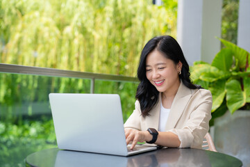 Freelance Asian business woman working using laptop computer. She sits and works in the public garden.