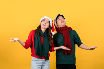 Obraz premium Photo of an excited Asian couple in Christmas clothes looking up with open hands on a yellow studio background.