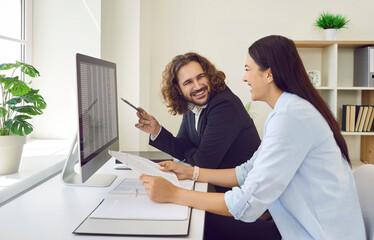 Obraz na płótnie Canvas Two young business smiling cheerful company employees man and woman having discussion and working at the desk in office on workplace looking to financial data. Accountant work concept.