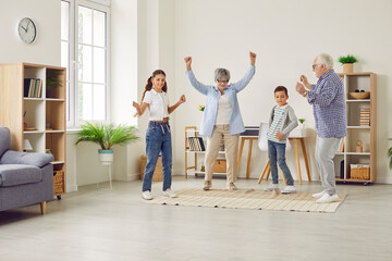 Full length portrait of a happy smiling senior grandparents having fun with their grandchildren brother and sister dancing in the living room at home enjoying weekend. Family leisure concept.