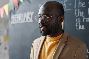 Close-up of African American teacher in eyeglasses talking at lecture against blackboard