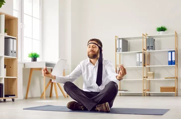 Foto op Plexiglas Funny business man or office worker in white shirt, with necktie around his head sitting with crossed legs on yoga mat on floor, doing meditation, relaxing and calming down on stressful day at work © Studio Romantic