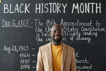 Portrait of history African American teacher smiling at camera standing against blackboard with...