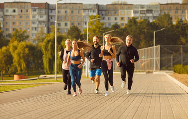 Team of young people men and women running together in the park having sport workout outdoors. Group of runners training in nature jogging in city park. Healthy lifestyle and fitness concept.