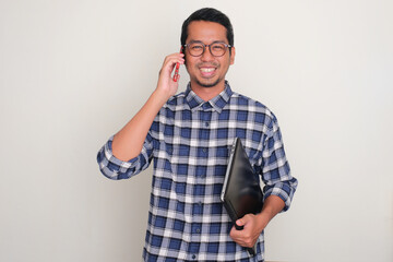 A man holding laptop smiling happy while answering a phone call