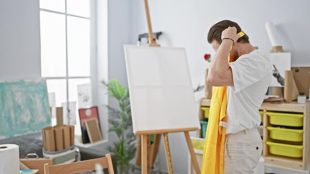 Young hispanic man artist wearing apron standing with serious face at art studio