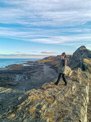 Obraz premium A woman on the background of the rocky coast of the Barents Sea. Beautiful view of the cliffs and the coast of the Rybachy and Sredny peninsulas. The harsh beauty of the north.