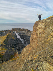 A woman on the background of the rocky coast of the Barents Sea. Beautiful view of the cliffs and the coast of the Rybachy and Sredny peninsulas. The harsh beauty of the north.