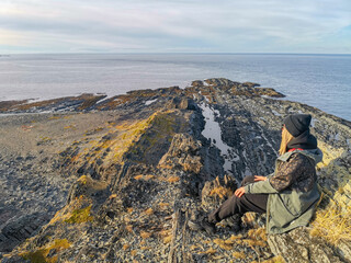 A woman on the background of the rocky coast of the Barents Sea. Beautiful view of the cliffs and the coast of the Rybachy and Sredny peninsulas. The harsh beauty of the north.