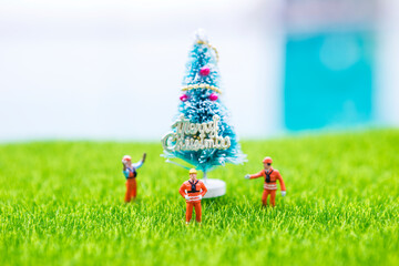 Miniature worker in safety suit with Christmas tree on green grass with space on blurred background, Happy Chirstmas card background idea, buy new Christmas tree