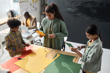 High angle view of school children making handicraft from colorful papers at table in team