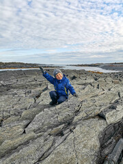 Fototapeta na wymiar A boy on the background of the rocky coast of the Barents Sea. Beautiful view of the cliffs and the coast of the Rybachy and Sredny peninsulas. The harsh beauty of the north.