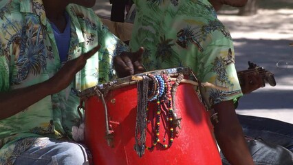 closeup of african american hands playing a red drum outdoors in the caribbean

