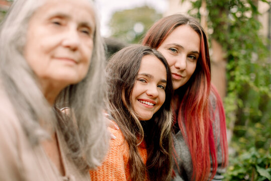 Portrait of smiling woman sitting with daughter and mother in backyard