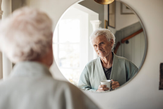 Senior man holding coffee cup while looking in mirror at home