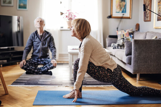 Senior woman and man practicing yoga together in living room at home