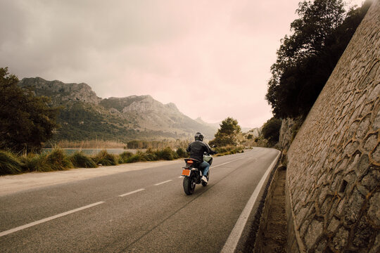 Man riding motorcycle on road in front of mountains aganist sky