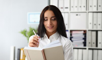 Beautiful woman smiles thoughtfully and holds pen and diary. Weekly planning and business plan