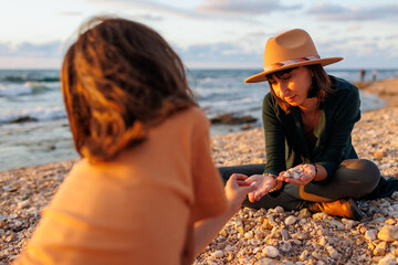 boy collects shells and pebbles in the sea on a sandy beach with his mother. Family having fun on the beach collecting shells.