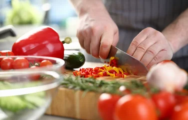 Fotobehang Hands of cook cut yellow and red peppers on cutting board with other vegetables on table in kitchen. Cooking fresh vitamin tasty salad concept © H_Ko