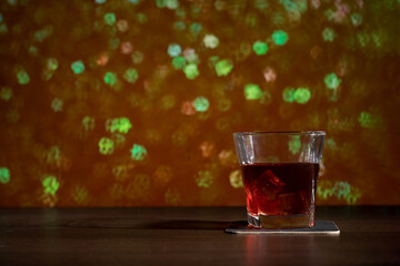 Glass of whiskey on the bar in front of the blur image Christmas background. Festive abstract background with bokeh defocused lights and stars