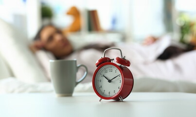 Red alarm clock at ten o'clock and sleeping woman. Peaceful sleep and late rise concept