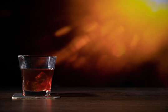 Glass of whiskey on the bar in front of the blur image Abstract Natural Sun flare on the black
