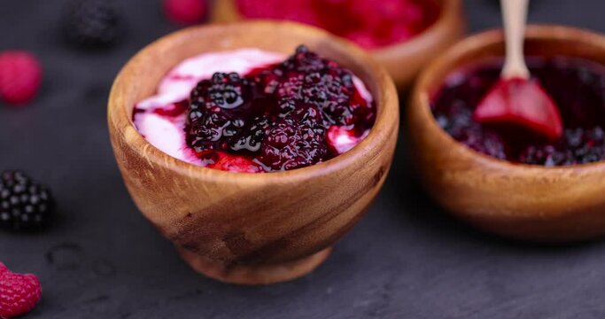 fresh yogurt with crushed juicy blackberries, preparation of yogurt desserts using juice and berries of ripe blackberries