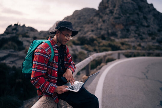 Male backpacker using laptop while sitting on railing at sunset