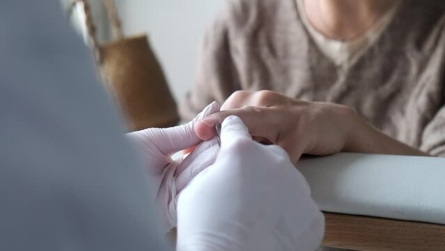 A manicurist wearing white gloves does his job. Manicure process in a beauty salon close-up. Cuticle removal. Self care concept.