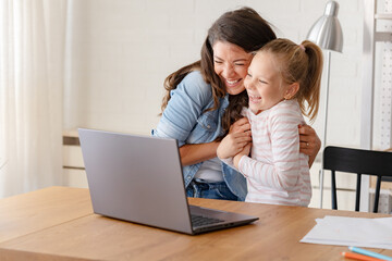 A cheerful mother and daughter engage in a video call over a laptop computer, sharing smiles and moments of connection