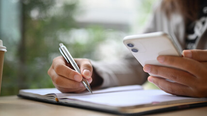 Cropped shot of businesswoman holding mobile phone and writing notes