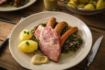 2 Portionen Oldenburger Grünkohl mit geräucherter Kohlwurst, Pinkel, Kassler Nacken, Kartoffeln, Senf, Petersilie auf Teller und Holz Hintergrund