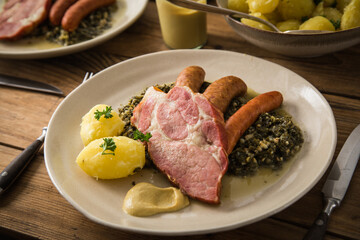 2 Portionen Oldenburger Grünkohl mit geräucherter Kohlwurst, Pinkel, Kassler Nacken, Kartoffeln, Senf, Petersilie auf Teller und Holz Hintergrund