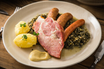 Oldenburger Grünkohl mit geräucherter Kohlwurst, Pinkel, Kassler Nacken, Kartoffeln, Senf, Petersilie auf Teller und Holz Hintergrund