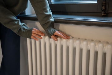 Woman warming hands near radiator at home after walking in cold winter weather, female touching...