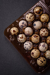 Raw quail eggs in a plastic box on a dark concrete background